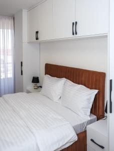 een bed met witte lakens en een houten hoofdeinde bij Nest Apartments in Gjakove