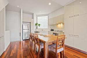 a white kitchen with a wooden table and chairs at Trendy 3 Level Retreat at North Melbourne with parking in Melbourne