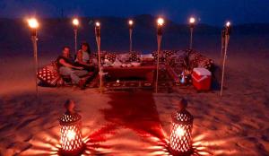 a couple sitting on a bed on the beach at night at Sam Safari Resort Jaisalmer in Jaisalmer