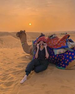 a woman sitting next to a camel in the desert at Sam Safari Resort Jaisalmer in Jaisalmer