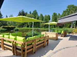 um pátio com cadeiras verdes e guarda-sóis em frente a um lago em Le Domaine du Cerf Blanc em Carentoir