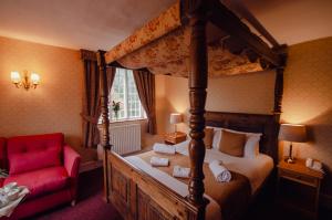 - une chambre avec un lit à baldaquin et une chaise rouge dans l'établissement Howfield Manor Hotel, à Canterbury