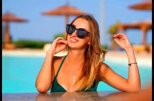 Juliana Beach Hurghada في الغردقة: امرأة ترتدي نظارة شمسية تجلس على طاولة بالقرب من مسبح