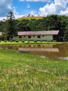 a white building with a red roof next to a pond at Pousada Água Santa in São Joaquim