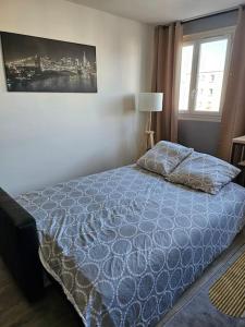 een slaapkamer met een bed met een blauw dekbed en een raam bij Appartement Art deco proche bords de Marne in Neuilly-sur-Marne