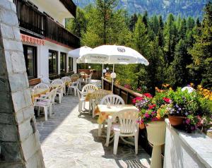 un patio con sedie e tavoli bianchi e ombrellone di Bellavista Schönblick a Casere Alte