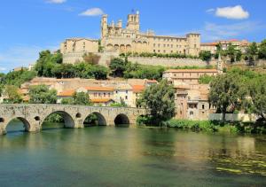 un pont sur une rivière avec un château en arrière-plan dans l'établissement Le Nid Canal Piscine Résidence, à Béziers