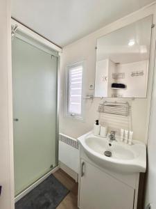 y baño blanco con lavabo y ducha. en Mobil Home Abricotiers 1, en Valras-Plage
