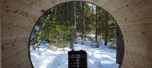 - une fenêtre ronde dans un bâtiment en bois avec une forêt enneigée dans l'établissement Charlevoix expérience thermale en pleine nature - Suites Nature Charlevoix - Suite #1, aux Éboulements