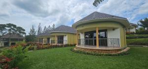 a yellow house with a porch on a green lawn at Kaije Country Cottages in Fort Portal