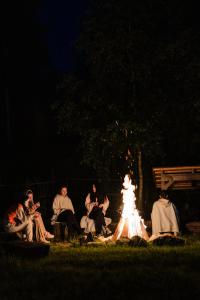 Un gruppo di persone sedute intorno al fuoco di notte di Raven's Nest - The Hidden Village, Transylvania - Romania a Sub Piatra