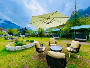 a group of chairs and a table with an umbrella at The Himalayan Cottage Camping With Bonfire, Manali - Riverside in Manāli