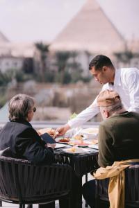 Een man die mensen bedient aan een tafel met eten. bij Tuya Pyramids Inn hotel in Caïro