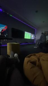 ein Zimmer mit einer Person, die auf einer Couch sitzt und einen TV sieht in der Unterkunft Club PlayStation “WarZone” Banjaluka in Banja Luka