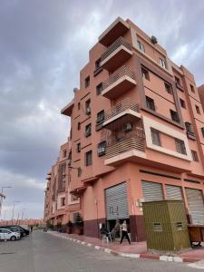 un edificio rosa alto con gente caminando delante de él en Résidence les Jardin d Anass Aéroport Marrakech, en Marrakech