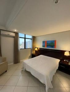 Manaus hotéis millennium flat في ماناوس: غرفة نوم بسرير ابيض ونافذة كبيرة