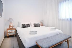 ein weißes Schlafzimmer mit einem großen Bett und einer Bank in der Unterkunft New Day by HolyGuest in Tel Aviv