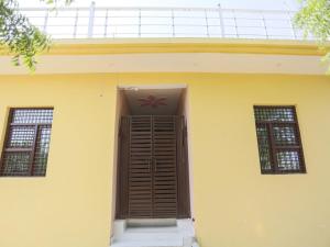 ein gelbes Haus mit brauner Tür und zwei Fenstern in der Unterkunft OYO Hotel Pari in Greater Noida