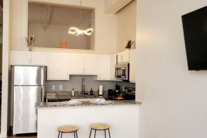 a kitchen with white cabinets and a refrigerator and two stools at Naranja Loft #5 FREE Parking & Skywalk to Lucas Oil & Conv Center in Indianapolis