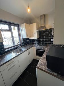a kitchen with white cabinets and a black appliance at Charlton, Greenwich Service Apartment in London