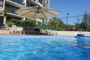 a swimming pool with an umbrella and chairs at Princess Palm on the Beach in Gold Coast