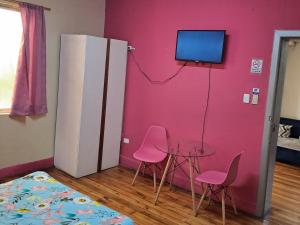 Habitación con 2 sillas rosas, mesa y TV. en Magic Hostal, en Quito