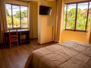 een slaapkamer met een bed, een bureau en ramen bij Hospedaje Cattleya in Oxapampa