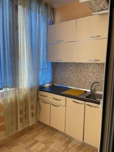 cocina con armarios blancos, lavamanos y cortinas azules en Квартира на пляже, en Durrës