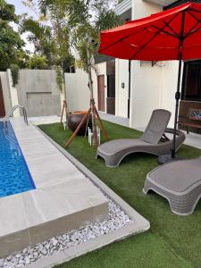 a pool with a red umbrella and chairs next to a house at Dano Private Resort and Apartments in Dauis
