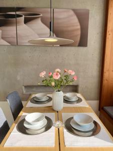 a table with plates and a vase with pink flowers at Paradies in den Südsteirischen Weinbergen: Bezauberndes Apartment mit Terrasse, Infinity Pool-Zugang, Sauna und Fitnessbereich! in Obegg