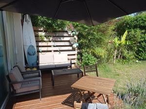 um guarda-chuva num deque com um sofá e uma mesa em Studio avec jardin à 2km de L'Océan ! em Labenne