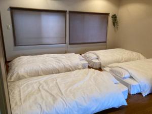 two beds in a room with white sheets at かつやま民泊きねん in Katsuyama