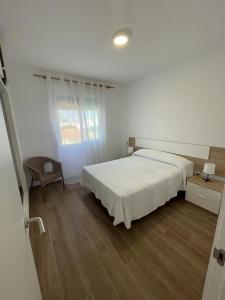 ein weißes Schlafzimmer mit einem Bett und einem Stuhl in der Unterkunft Apartamento cerca de la playa in Vinarós