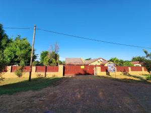 a dirt road with a red fence and a house at COMFORT ZONE GUEST HOUSE in Zeerust