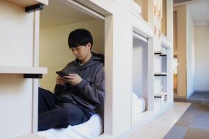 Un garçon assis dans une fenêtre qui regarde son téléphone portable dans l'établissement Hotel Tomariya Ueno, à Tokyo