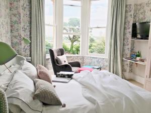 a bedroom with a bed and a chair and windows at The Firs Boutique Bed and Breakfast, St Ives, Cornwall in St Ives