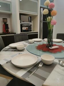 uma mesa de jantar com pratos brancos e flores num vaso em Deli Villa em Muar