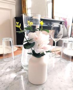 eine weiße Vase mit Blumen auf einem Tisch mit Brille in der Unterkunft Le Carré Bleu - Studio Confort - Centre-ville in Dieppe
