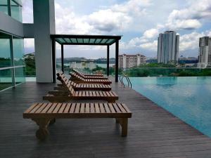 une rangée de bancs en bois assis sur une terrasse à côté d'une piscine dans l'établissement Paragon Suites Holiday Short gateway Jacuzzi CIQ, à Johor Bahru