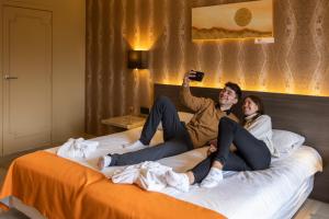 Ein Mann und eine Frau, die auf einem Bett sitzen und ein Foto machen. in der Unterkunft Hotel Donny in De Panne