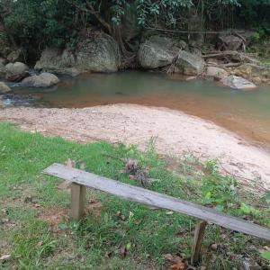 un banco de madera sentado junto a un cuerpo de agua en Camping Casa Velha, en Guarapari
