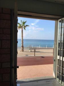 een open deur naar een strand met een palmboom bij Appartamento sul mare (Ventimiglia/Bordighera) in Vallecrosia
