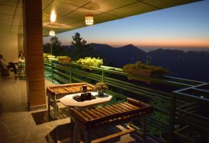 una mesa y 2 bancos en un balcón con vistas en Nature Mountain Valley View Resort -- A Four Star Luxury Resort en Shimla