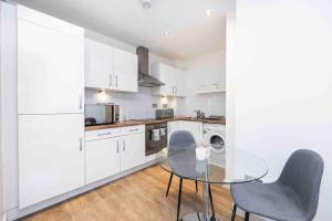 uma cozinha com armários brancos, uma mesa de vidro e cadeiras em Stylish 1 BR Apartment Near Shoreditch - 10 Min Walk em Londres