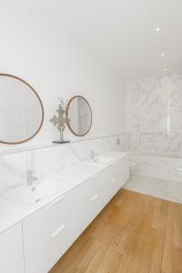 a white bathroom with two sinks and two mirrors at Appartement sur les quais in Paris