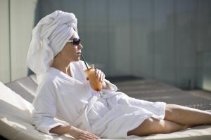a woman in a white robe sitting on a bed at Hotel Zena Beauty & Shopping Center in Hévíz