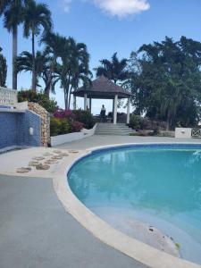 a large swimming pool with a gazebo and palm trees at Refreshed Modern Country Feel Apartment in Ocho Rios