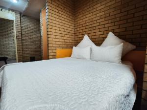 a bedroom with a white bed with a brick wall at Orlando Hotel in Soweto
