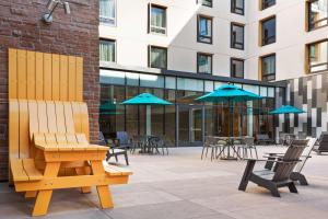 eine Bank vor einem Gebäude mit Tischen und Sonnenschirmen in der Unterkunft Hilton Garden Inn Boulder in Boulder