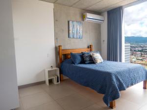 a bedroom with a bed with a blue blanket and a window at iFreses, Lofts Full equipped whith Pool, air-conditioning, spectacular view of the city in Curridabat